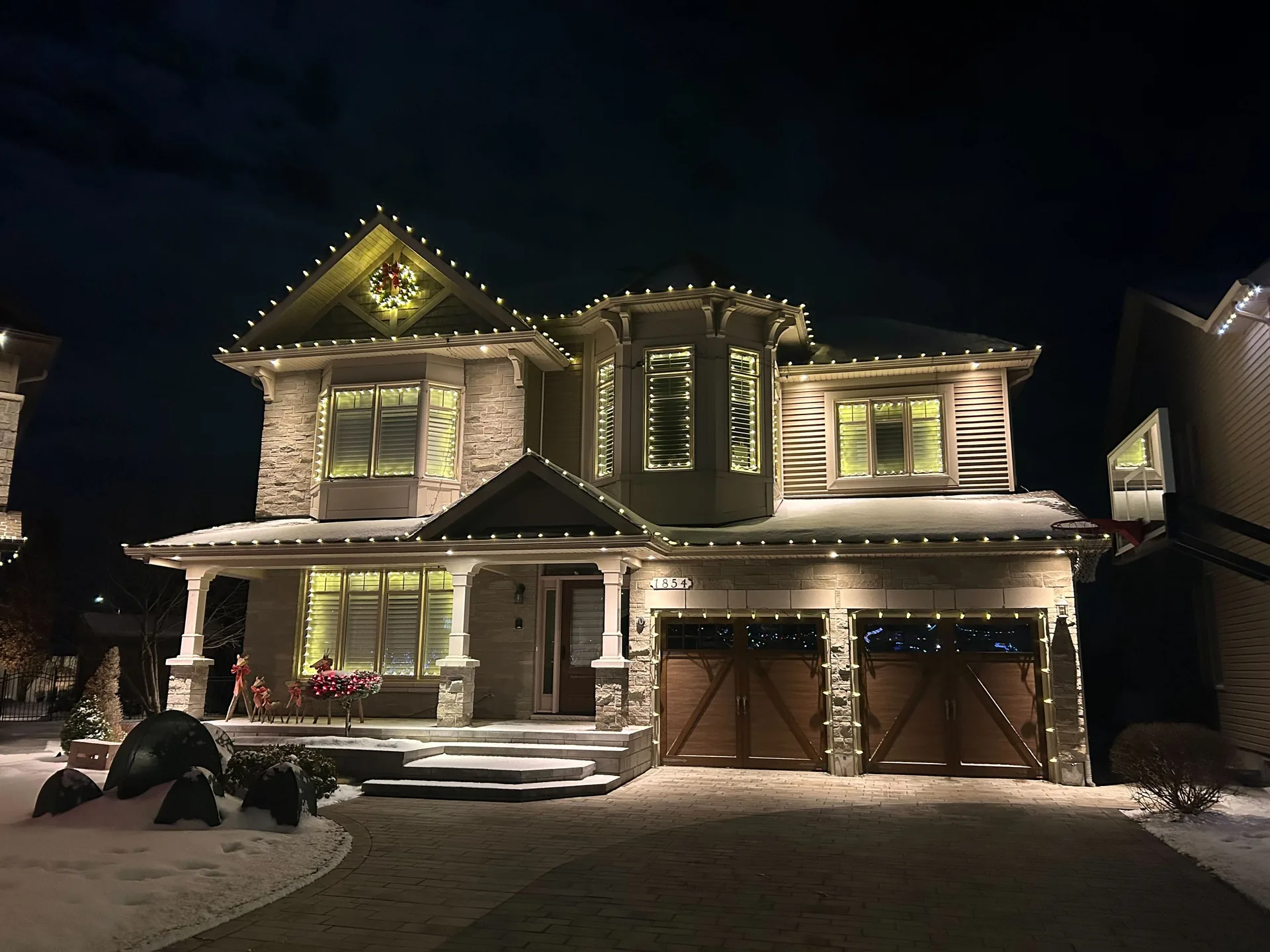 Professional warm-white roofline Christmas lights, wreath, and window lighting on an Ottawa home at night